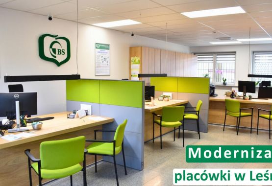 Trzy osoby siedzące przy drewnianym stole – doradczyni bankowa w czarnym żakiecie oraz para klientów. Na stole leżą dokumenty i otwarty laptop, a doradczyni wskazuje coś na ekranie smartfona. W lewym górnym rogu logotyp Banku Spółdzielczego w Leśnicy. Na dole napis: „Oszczędności. Dlaczego warto mieć finansową poduszkę bezpieczeństwa?”