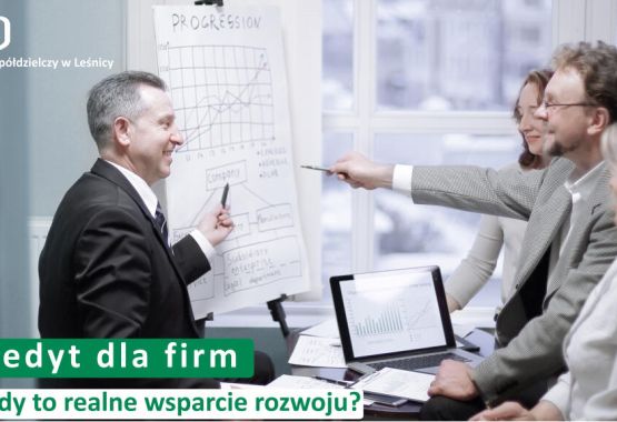 Trzy osoby siedzące przy drewnianym stole – doradczyni bankowa w czarnym żakiecie oraz para klientów. Na stole leżą dokumenty i otwarty laptop, a doradczyni wskazuje coś na ekranie smartfona. W lewym górnym rogu logotyp Banku Spółdzielczego w Leśnicy. Na dole napis: „Oszczędności. Dlaczego warto mieć finansową poduszkę bezpieczeństwa?”